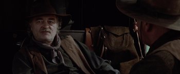 Movie still from “Unforgiven” (1992), directed by Clint Eastwood – A man sitting in a chair wearing a cowboy hat; Close Up shot, Over the shoulder angle