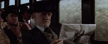 Movie still from “Unforgiven” (1992), directed by Clint Eastwood – An older man sitting on a train holding a newspaper; Close Up shot, Over the shoulder angle