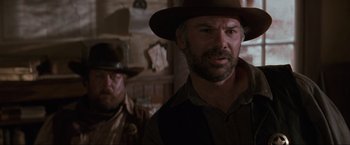 Movie still from “Unforgiven” (1992), directed by Clint Eastwood – A man with a hat and a beard standing next to another man in a hat; Close Up shot, Over the shoulder angle
