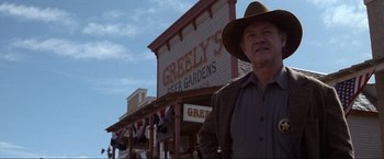 Movie still from “Unforgiven” (1992), directed by Clint Eastwood – A man standing in front of a building with people in front of it; Medium shot, Low angle