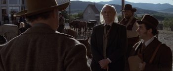 Movie still from “Unforgiven” (1992), directed by Clint Eastwood – A man in a suit standing in front of a group of horses; Medium shot, Over the shoulder angle