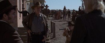 Movie still from “Unforgiven” (1992), directed by Clint Eastwood – A group of people in a field with a gun; Medium shot, Over the shoulder angle