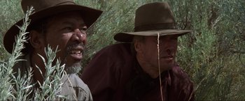 Movie still from “Unforgiven” (1992), directed by Clint Eastwood – Two men in hats are standing next to each other in the woods; Close Up shot, Low angle