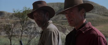 Movie still from “Unforgiven” (1992), directed by Clint Eastwood – Two men in hats and a beard standing next to each other on a hill; Close Up shot, Low angle