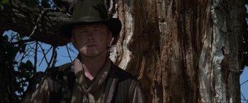 Movie still from “Unforgiven” (1992), directed by Clint Eastwood – A man wearing a hat standing in front of a tree; Close Up shot, Low angle