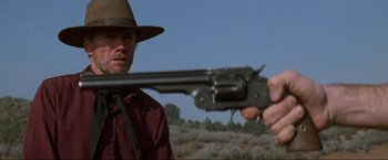 Movie still from “Unforgiven” (1992), directed by Clint Eastwood – A man in a hat is holding a gun; Close Up shot, Over the shoulder angle