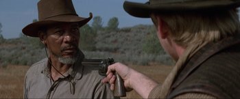Movie still from “Unforgiven” (1992), directed by Clint Eastwood – A man holding a gun pointed at another man's face; Close Up shot, Over the shoulder angle