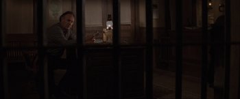 Movie still from “Unforgiven” (1992), directed by Clint Eastwood – A man sitting at a table in a dark room; Medium shot, High angle