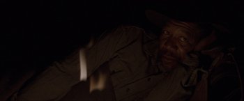 Movie still from “Unforgiven” (1992), directed by Clint Eastwood – A man with a beard and a cowboy hat is in the dark; Close Up shot, High angle