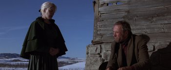 Movie still from “Unforgiven” (1992), directed by Clint Eastwood – A man and a woman sitting in front of a wooden structure; Medium shot, Low angle