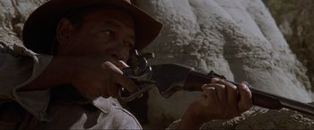 Movie still from “Unforgiven” (1992), directed by Clint Eastwood – A man in a hat holding an old - fashioned gun; Close Up shot, Low angle