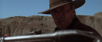 Movie still from “Unforgiven” (1992), directed by Clint Eastwood – A man in a hat is holding a rifle; Close Up shot, Low angle