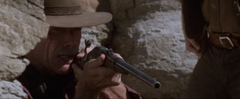 Movie still from “Unforgiven” (1992), directed by Clint Eastwood – A man holding a gun while wearing a cowboy hat; Close Up shot, Low angle