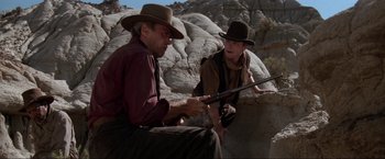 Movie still from “Unforgiven” (1992), directed by Clint Eastwood – Two men sitting next to each other holding guns; Medium shot, Low angle