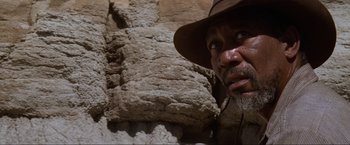 Movie still from “Unforgiven” (1992), directed by Clint Eastwood – A man in a hat and a hat stands in front of a rock wall; Close Up shot, Low angle