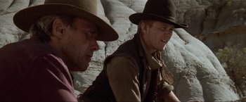 Movie still from “Unforgiven” (1992), directed by Clint Eastwood – A man in a cowboy hat sitting next to another man in a cowboy hat; Close Up shot, Over the shoulder angle