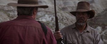 Movie still from “Unforgiven” (1992), directed by Clint Eastwood – A man holding a rifle while standing next to another man; Close Up shot, Over the shoulder angle