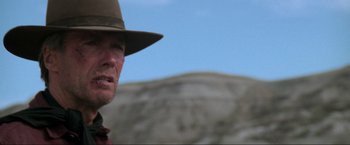 Movie still from “Unforgiven” (1992), directed by Clint Eastwood – A man wearing a hat standing in front of a mountain; Close Up shot, Low angle