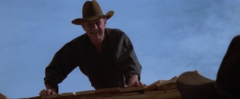 Movie still from “Unforgiven” (1992), directed by Clint Eastwood – An older man wearing a cowboy hat is working on a roof; Medium shot, Low angle