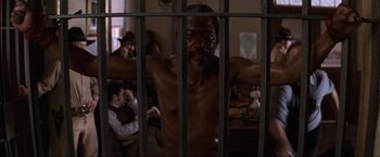 Movie still from “Unforgiven” (1992), directed by Clint Eastwood – A man standing behind bars in a room; Medium shot, Low angle