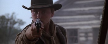 Movie still from “Unforgiven” (1992), directed by Clint Eastwood – A man holding a gun while wearing a cowboy hat; Close Up shot, Low angle