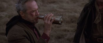 Movie still from “Unforgiven” (1992), directed by Clint Eastwood – A man drinking a beer from a glass bottle; Close Up shot, High angle
