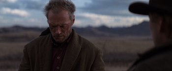 Movie still from “Unforgiven” (1992), directed by Clint Eastwood – An older man with a bruised eye is standing in a field; Close Up shot, Over the shoulder angle