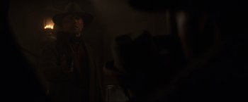 Movie still from “Unforgiven” (1992), directed by Clint Eastwood – A man wearing a hat and a long coat is standing in a dark room; Medium shot, Over the shoulder angle