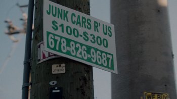 Movie still from “Untrapped: The Story of Lil Baby” (2022), directed by Karam Gill – A sign on the side of a pole that says junk cars r ' us for $ 1 0 0 -$ 3 0 0; Extreme Close Up shot, Low angle