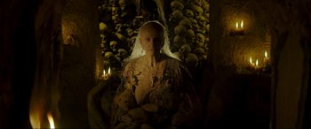 Movie still from “Unwelcome” (2022), directed by Jon Wright – An old woman with a white veil in front of a wall full of skulls; Medium shot, Low angle