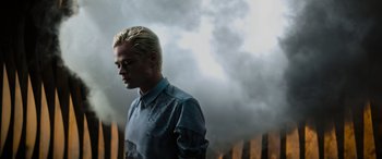 Movie still from “Upgrade” (2018), directed by Leigh Whannell – A man with blonde hair standing in front of a wall of fire; Medium shot, Low angle