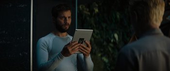 Movie still from “Upgrade” (2018), directed by Leigh Whannell – A man holding an ipad while standing in front of a tree; Close Up shot, Low angle