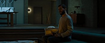Movie still from “Upgrade” (2018), directed by Leigh Whannell – A man sitting on a couch holding a box; Medium shot, Over the shoulder angle