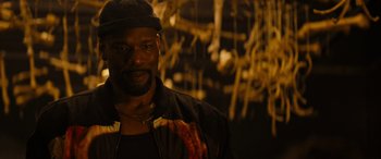 Movie still from “Upgrade” (2018), directed by Leigh Whannell – A man with a beard and a hat is standing in front of a wall; Close Up shot, Over the shoulder angle