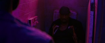 Movie still from “Upgrade” (2018), directed by Leigh Whannell – A man sitting in a bathroom in a purple light; Medium shot, Over the shoulder angle
