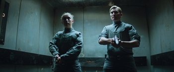 Movie still from “Upgrade” (2018), directed by Leigh Whannell – A man and a woman standing next to each other holding guns; Medium shot, Low angle