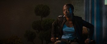 Movie still from “Upgrade” (2018), directed by Leigh Whannell – A woman in a leather jacket sitting in front of a tree; Medium shot, Over the shoulder angle