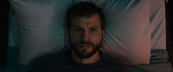 Movie still from “Upgrade” (2018), directed by Leigh Whannell – A bearded man laying in a bed with a pillow; Close Up shot, Overhead angle