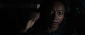 Movie still from “Upgrade” (2018), directed by Leigh Whannell – A woman is looking at the camera in the dark; Close Up shot, Over the shoulder angle