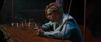 Movie still from “Upgrade” (2018), directed by Leigh Whannell – A man sitting at a table with a glass in front of him; Medium shot, Low angle