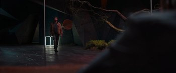 Movie still from “Upgrade” (2018), directed by Leigh Whannell – A man holding an umbrella walking in a dark room; Wide shot, Over the shoulder angle