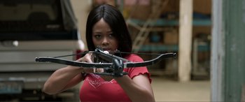 Movie still from “V for Vengeance” (2022), directed by Kelly Halihan – A woman holding a bow and arrow in a room; Medium shot, Over the shoulder angle