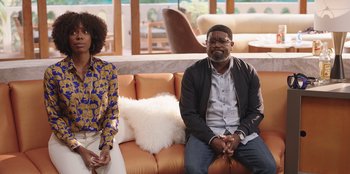 Movie still from “Vacation Friends” (2021), directed by Clay Tarver – A man and a woman sitting on a couch in a living room; Medium shot, Over the shoulder angle