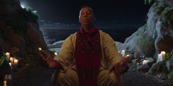 Movie still from “Vacation Friends” (2021), directed by Clay Tarver – A man sitting on the ground with his eyes closed; Medium shot, Low angle