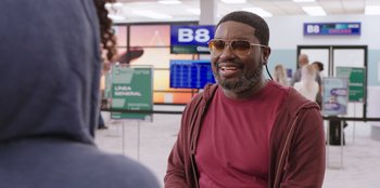 Movie still from “Vacation Friends” (2021), directed by Clay Tarver – A man in a red shirt and sunglasses is smiling; Close Up shot, Over the shoulder angle