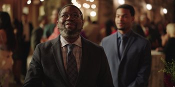 Movie still from “Vacation Friends” (2021), directed by Clay Tarver – A man in a suit standing next to another man in a suit; Medium shot, Over the shoulder angle