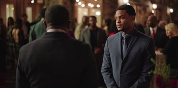 Movie still from “Vacation Friends” (2021), directed by Clay Tarver – A man in a suit and tie standing next to another man in a suit and tie; Medium shot, Over the shoulder angle