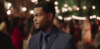 Movie still from “Vacation Friends” (2021), directed by Clay Tarver – A man wearing a suit and tie in front of a crowd; Close Up shot, Over the shoulder angle