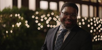 Movie still from “Vacation Friends” (2021), directed by Clay Tarver – A man in a suit and tie smiling for the camera; Close Up shot, Over the shoulder angle