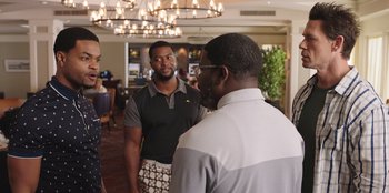 Movie still from “Vacation Friends” (2021), directed by Clay Tarver – A group of men standing around in a room; Medium shot, Over the shoulder angle